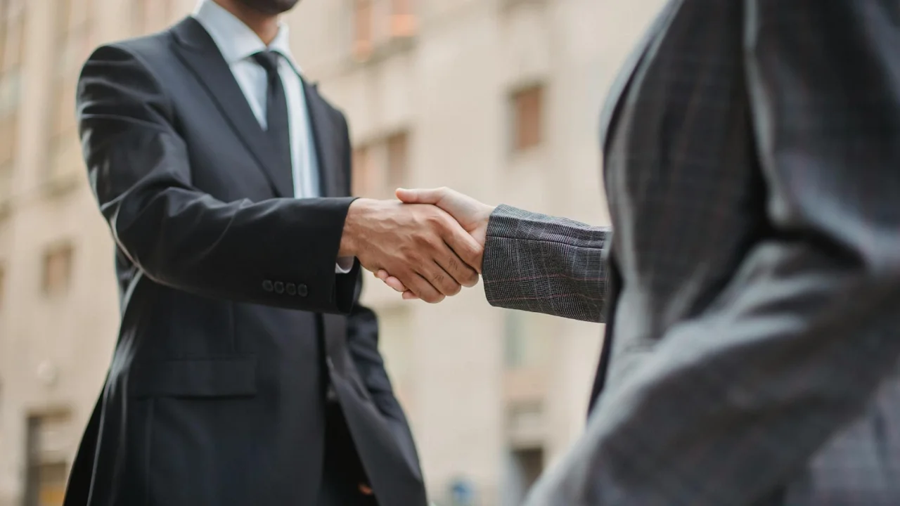 Επαγγελματίες χαιρετιούνται με χειραψία σε εξωτερικό χώρο, συμβολίζοντας τη συνεργασία.