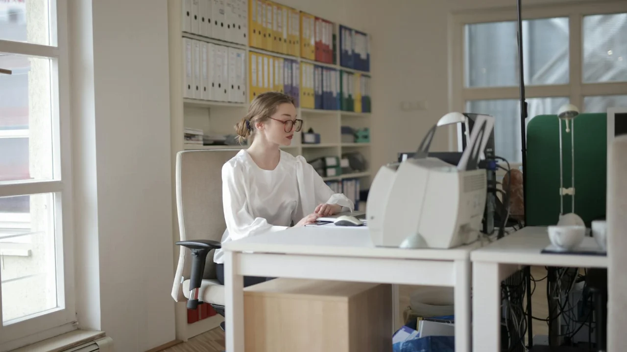 Focused woman working in a modern office filled with files and equipment.